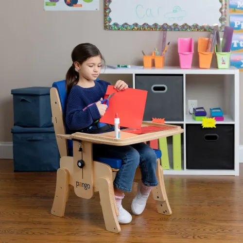 Child sitting on a Pango Activity Classroom Chair by Circle Specialty cutting red paper at a wooden desk